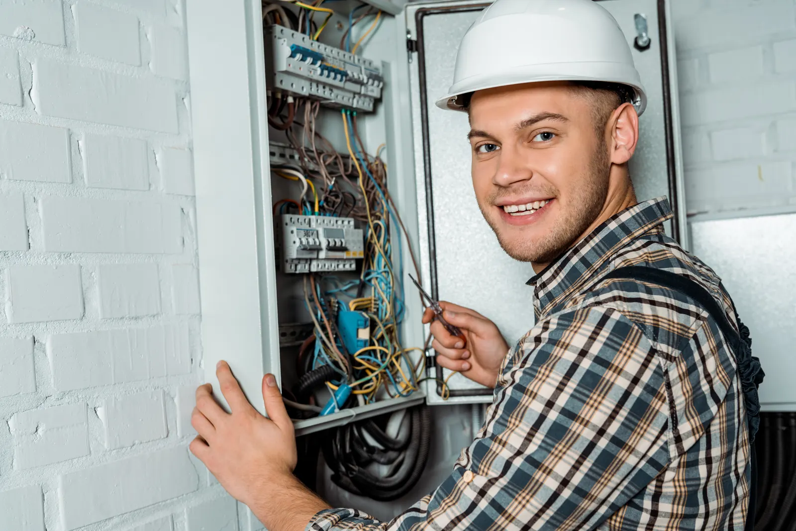 Elektriker mit Schutzhelm arbeitet an einem geöffneten Schaltschrank